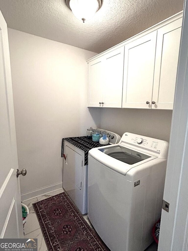 laundry room with washer and dryer, a textured ceiling, dark tile patterned floors, and cabinets