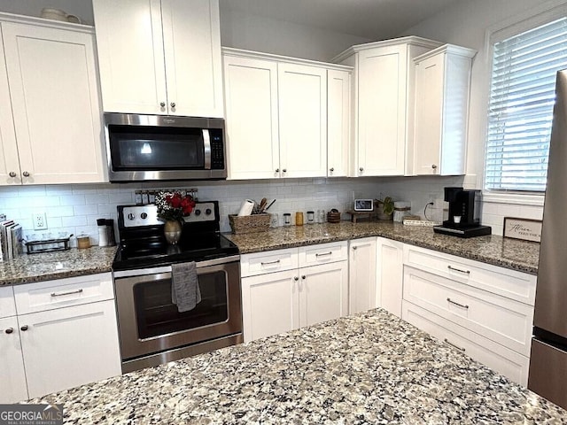 kitchen with white cabinets, backsplash, dark stone countertops, and stainless steel appliances