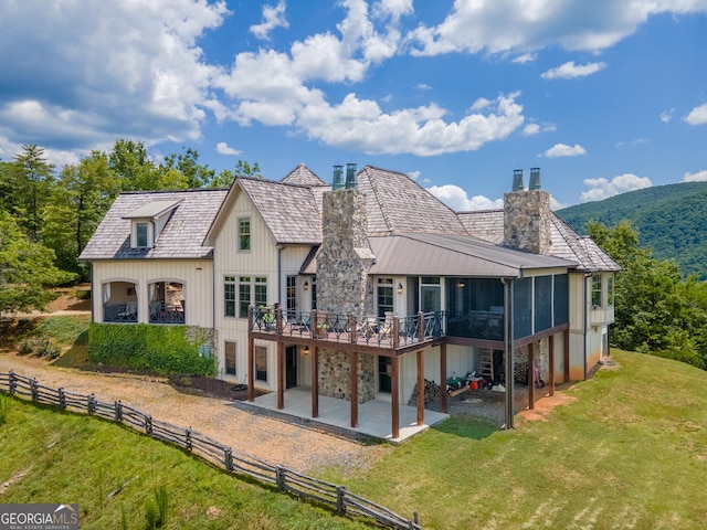 back of house featuring a lawn, a sunroom, a patio area, and a deck with mountain view