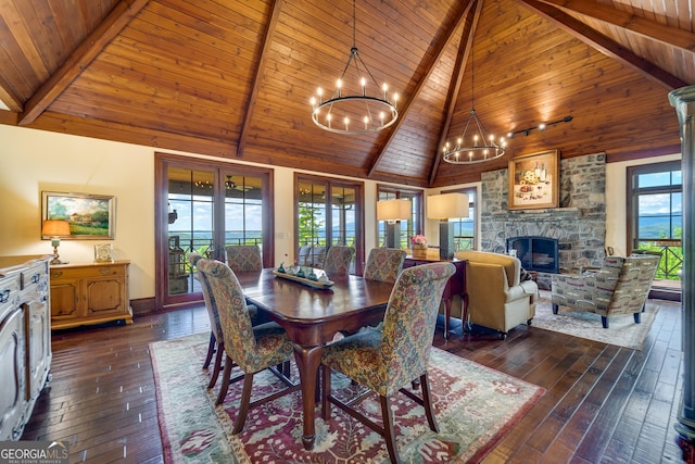 dining room with wood ceiling, dark wood-type flooring, beam ceiling, a notable chandelier, and a stone fireplace