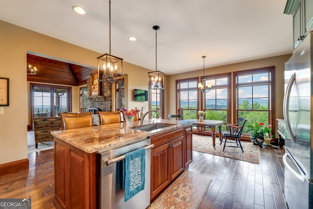 kitchen with a center island with sink, hanging light fixtures, sink, light stone countertops, and appliances with stainless steel finishes