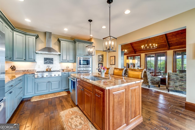 kitchen with sink, wall chimney exhaust hood, pendant lighting, a center island with sink, and appliances with stainless steel finishes