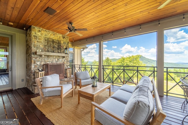 sunroom / solarium with a stone fireplace, a mountain view, ceiling fan, and wood ceiling