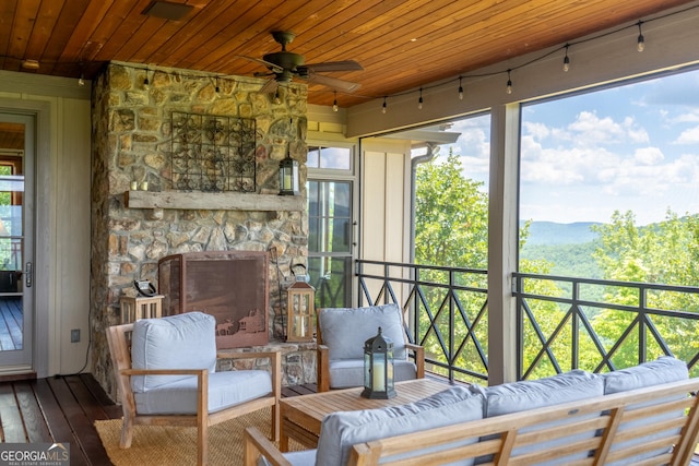 sunroom with a stone fireplace, ceiling fan, and wooden ceiling