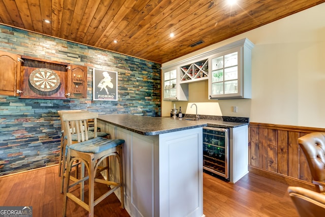 bar with white cabinetry, sink, beverage cooler, and wood-type flooring