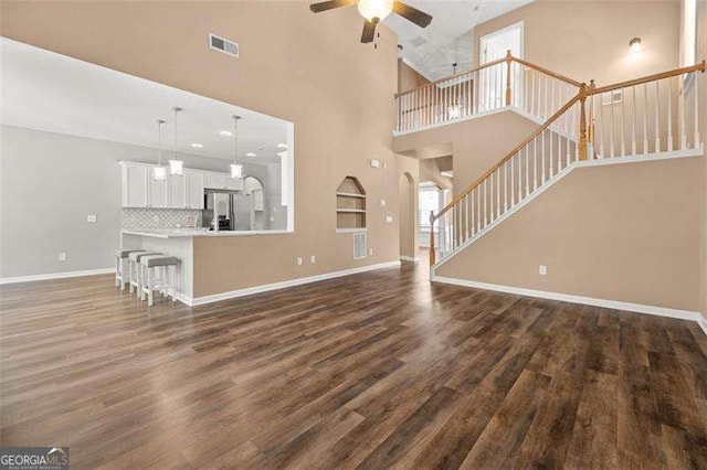 unfurnished living room with ceiling fan, a towering ceiling, and dark hardwood / wood-style floors