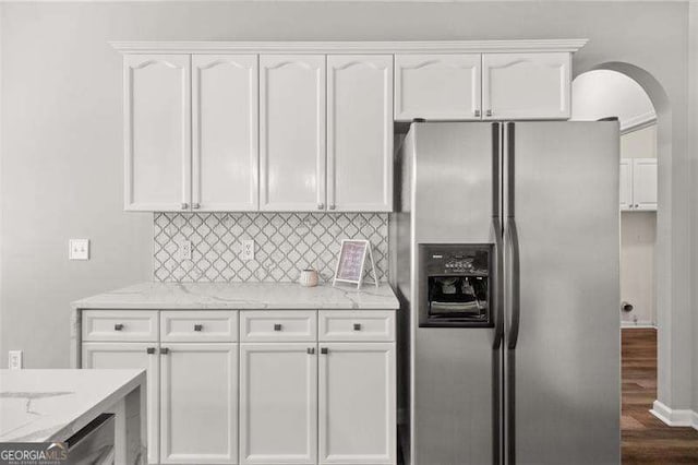 kitchen with stainless steel fridge, light stone counters, white cabinetry, and backsplash