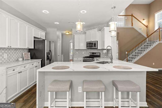 kitchen with white cabinets, sink, appliances with stainless steel finishes, decorative light fixtures, and light stone counters