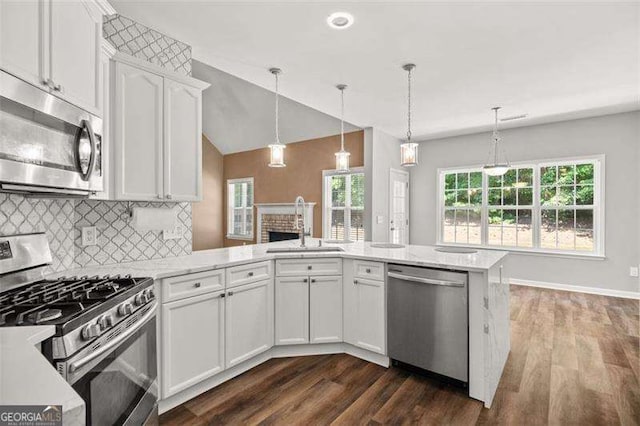 kitchen featuring kitchen peninsula, stainless steel appliances, sink, white cabinets, and hanging light fixtures