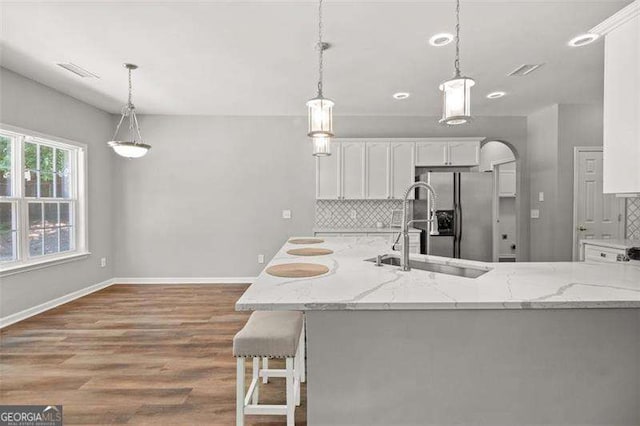 kitchen featuring light stone countertops, sink, hanging light fixtures, backsplash, and white cabinets