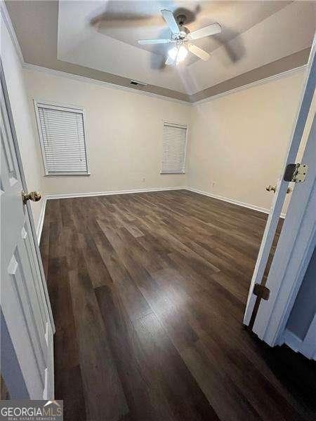 spare room featuring dark hardwood / wood-style floors, ceiling fan, ornamental molding, and a tray ceiling