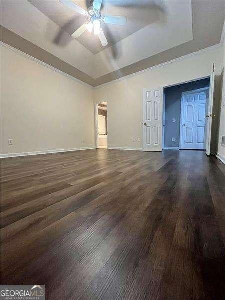 unfurnished living room featuring a tray ceiling, ceiling fan, and dark wood-type flooring