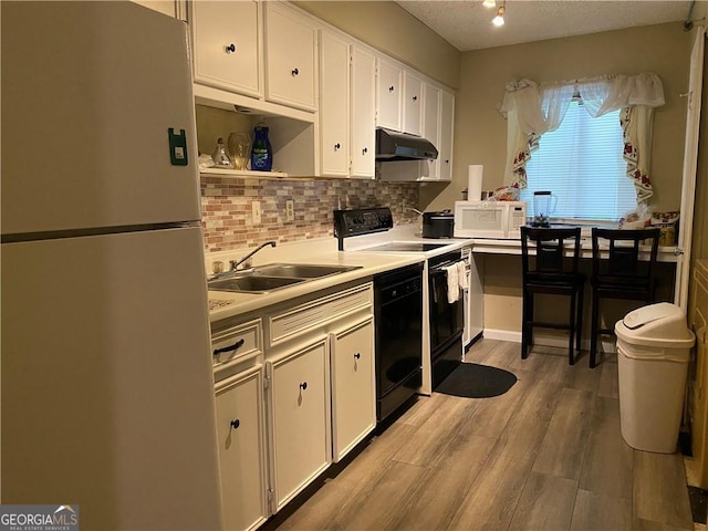 kitchen with sink, white cabinets, black appliances, and light wood-type flooring