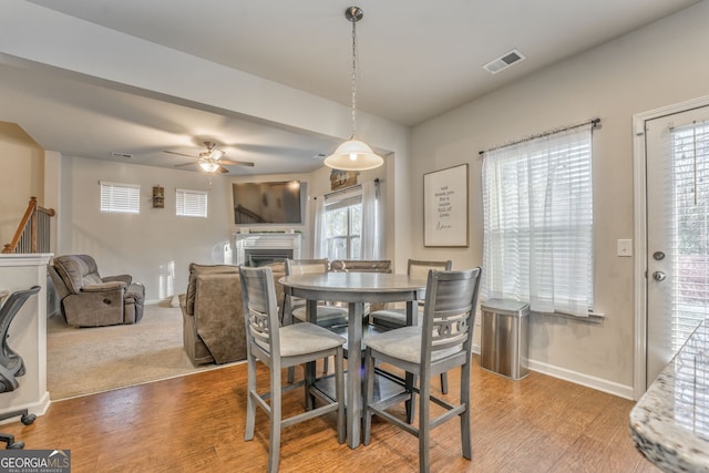 dining space featuring visible vents, a fireplace, baseboards, and wood finished floors