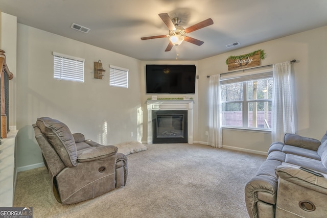 living room featuring a ceiling fan, visible vents, carpet flooring, and a glass covered fireplace