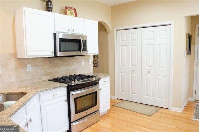 kitchen featuring white cabinets, decorative backsplash, light stone countertops, appliances with stainless steel finishes, and light hardwood / wood-style floors