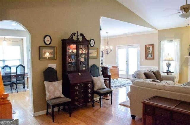 living room with french doors, ceiling fan with notable chandelier, vaulted ceiling, ornamental molding, and light hardwood / wood-style floors