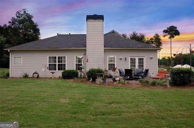 back house at dusk featuring french doors and a lawn