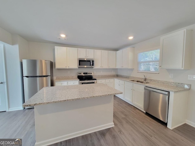 kitchen with white cabinets, stainless steel appliances, a center island, light stone countertops, and sink