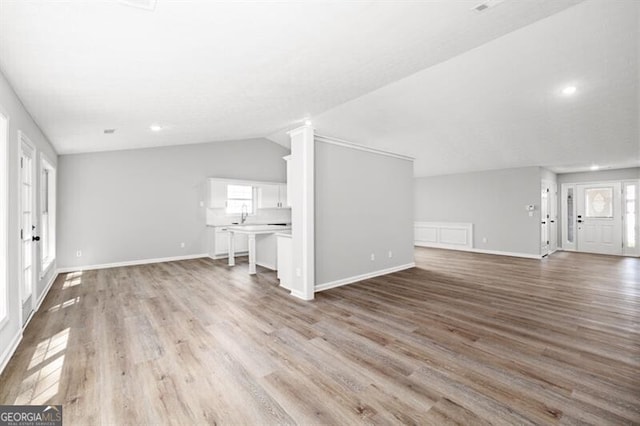 unfurnished living room with vaulted ceiling, french doors, sink, and light hardwood / wood-style flooring