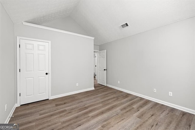 unfurnished bedroom with a textured ceiling, vaulted ceiling, and hardwood / wood-style flooring