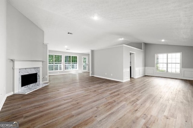 unfurnished living room with a fireplace, a textured ceiling, light wood-type flooring, and lofted ceiling