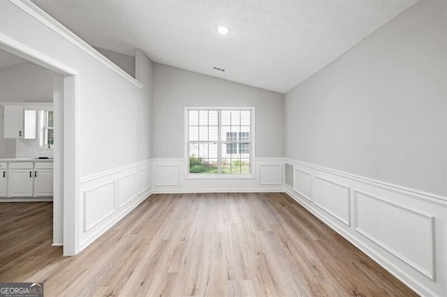 empty room with a textured ceiling, light wood-type flooring, and vaulted ceiling