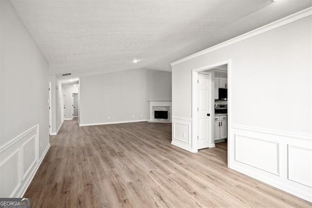 unfurnished living room with a high end fireplace, ornamental molding, a textured ceiling, vaulted ceiling, and light hardwood / wood-style floors