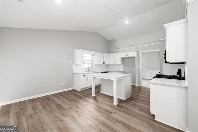 kitchen featuring white cabinetry, sink, backsplash, vaulted ceiling, and a kitchen island