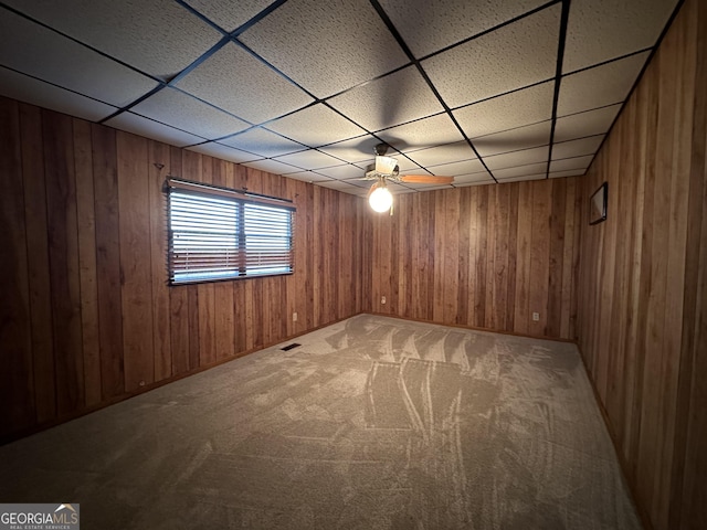 carpeted spare room with a drop ceiling and wooden walls