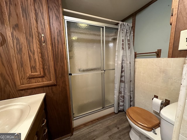 bathroom featuring hardwood / wood-style floors, a shower with door, toilet, and tile walls