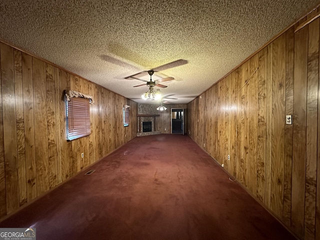 empty room with a textured ceiling, carpet floors, ceiling fan, and wooden walls