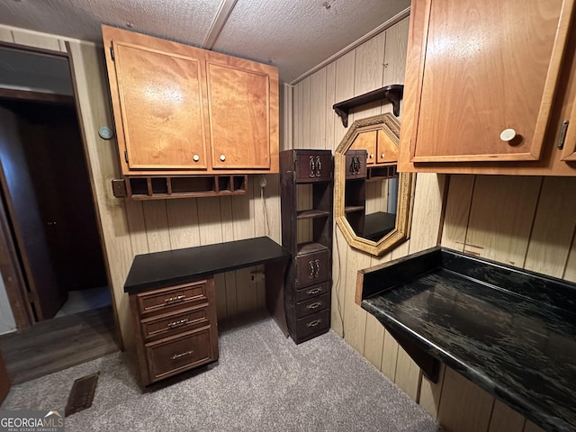 kitchen featuring a textured ceiling, dark carpet, and wood walls