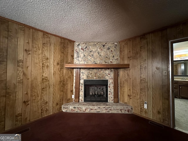 unfurnished living room with a textured ceiling, carpet, a fireplace, and wooden walls