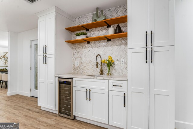 kitchen with white cabinets, sink, tasteful backsplash, light stone counters, and beverage cooler