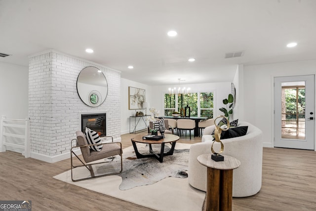 living room featuring a brick fireplace, light hardwood / wood-style flooring, and a notable chandelier