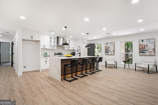 kitchen featuring stainless steel range with electric stovetop, white cabinets, light hardwood / wood-style floors, hanging light fixtures, and an island with sink