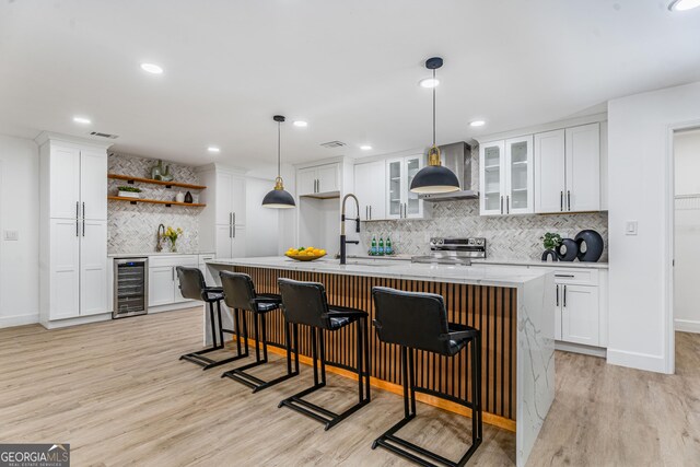 kitchen with white cabinetry, wine cooler, stainless steel electric range oven, and a kitchen island with sink