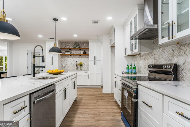 kitchen with pendant lighting, wall chimney exhaust hood, white cabinets, and stainless steel appliances