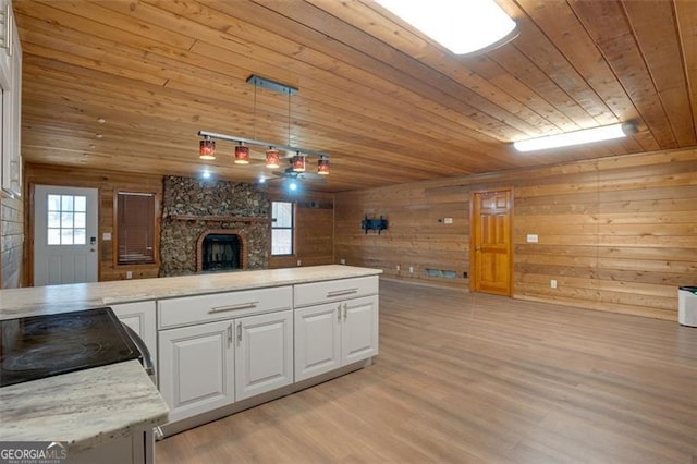 kitchen featuring a stone fireplace, white cabinetry, hanging light fixtures, and wood ceiling