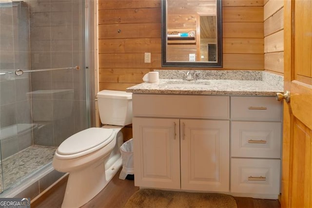 bathroom with wood walls, vanity, a shower with shower door, and toilet