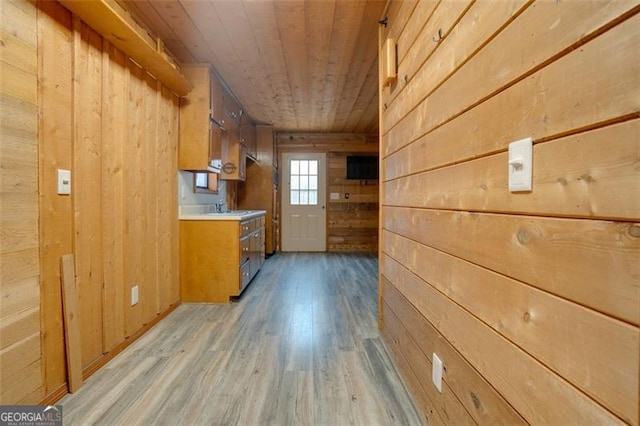 kitchen with wooden ceiling, sink, wooden walls, and light hardwood / wood-style flooring