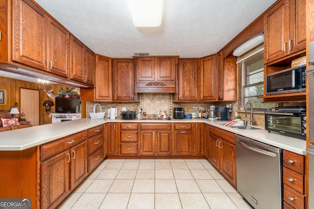 kitchen with sink, kitchen peninsula, a textured ceiling, decorative backsplash, and appliances with stainless steel finishes