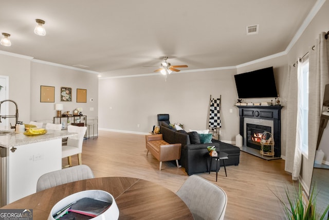 living room with sink, crown molding, light hardwood / wood-style floors, and a premium fireplace