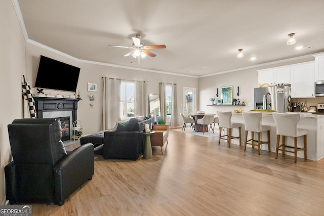 living room with ornamental molding, ceiling fan, and light hardwood / wood-style flooring