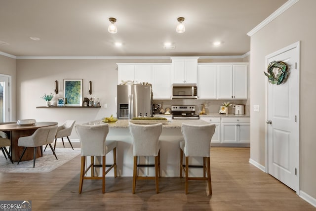 kitchen with a kitchen island with sink, stainless steel appliances, light stone counters, ornamental molding, and white cabinets