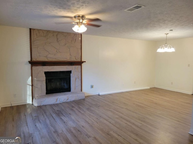 unfurnished living room featuring a fireplace, hardwood / wood-style floors, a textured ceiling, and ceiling fan with notable chandelier