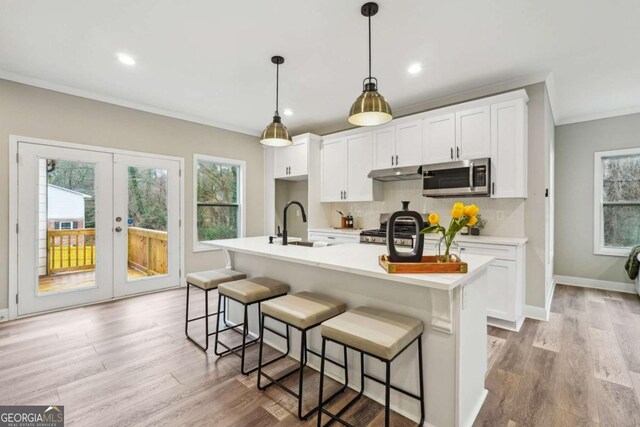 kitchen with pendant lighting, french doors, an island with sink, white cabinetry, and stainless steel appliances