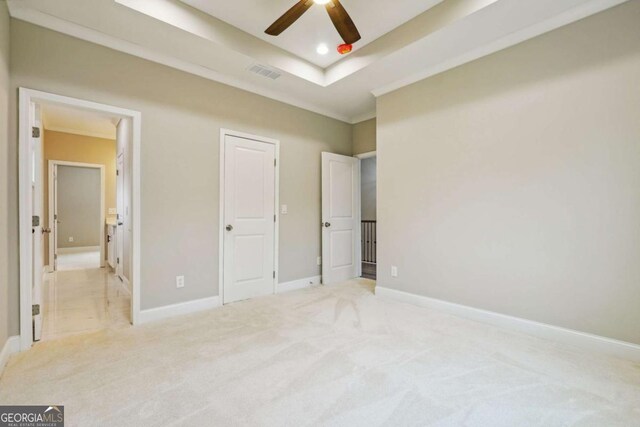 unfurnished bedroom with a tray ceiling, ceiling fan, and light carpet