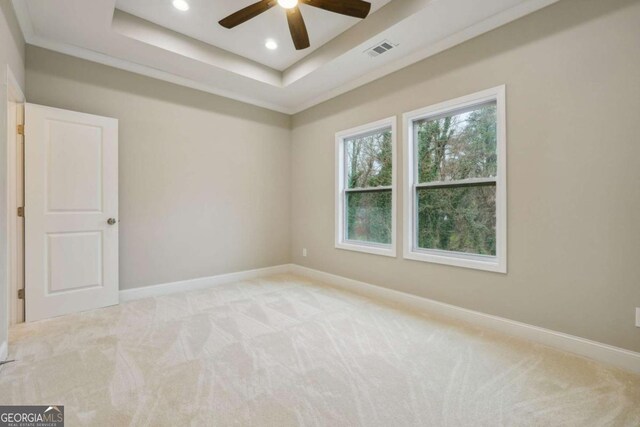 unfurnished room with a tray ceiling, light carpet, ceiling fan, and ornamental molding